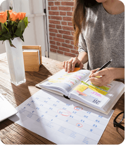 Femme écrivant dans un carnet avec un calendrier au dessus